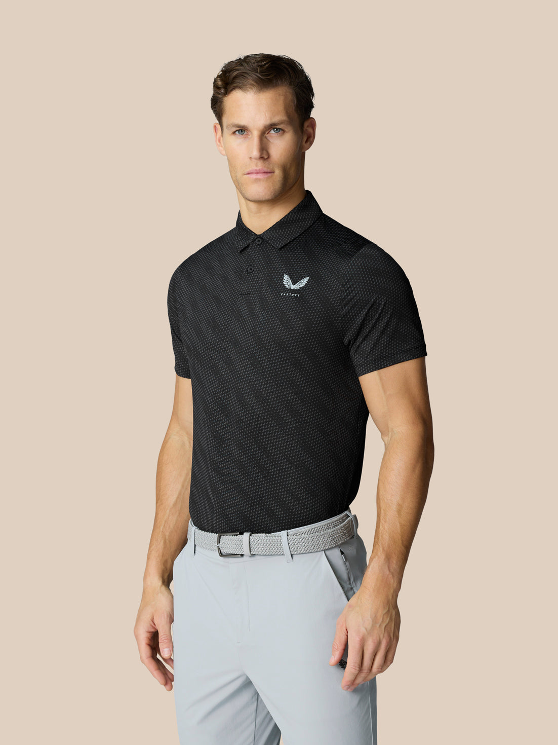 Male model wearing black Club Graphic Polo with golf ball pattern and Castore logo on the chest.