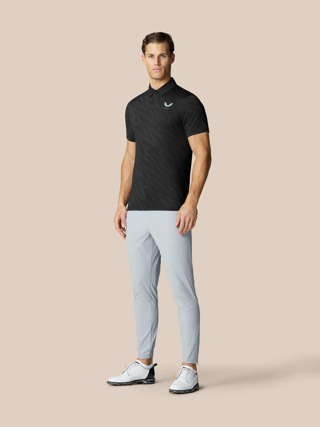 Man modeling Club Graphic Polo Black with dotted texture paired with light gray pants and white golf shoes