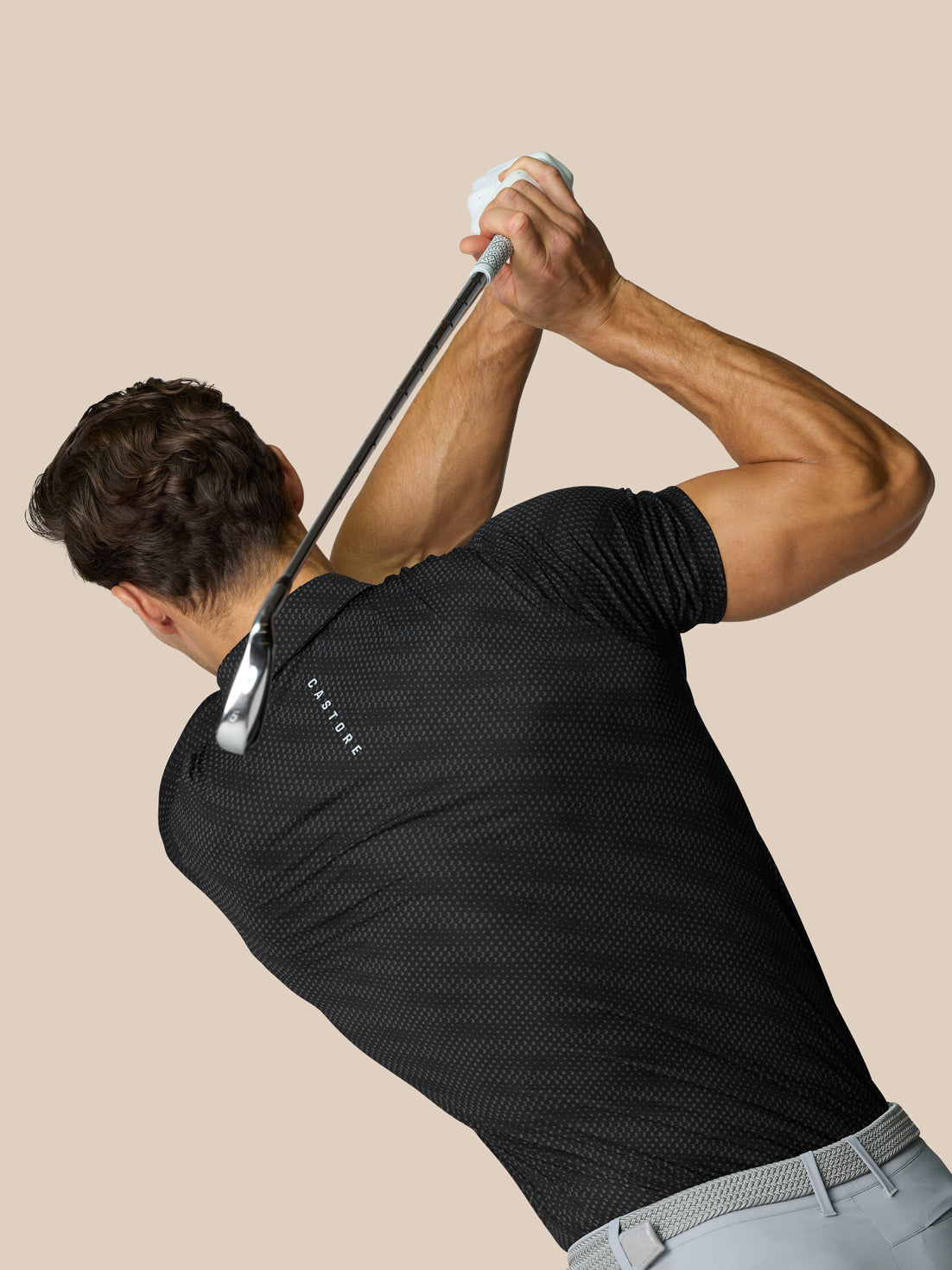 Male model wearing Club Graphic Polo Black with dotted texture during backswing holding a golf club