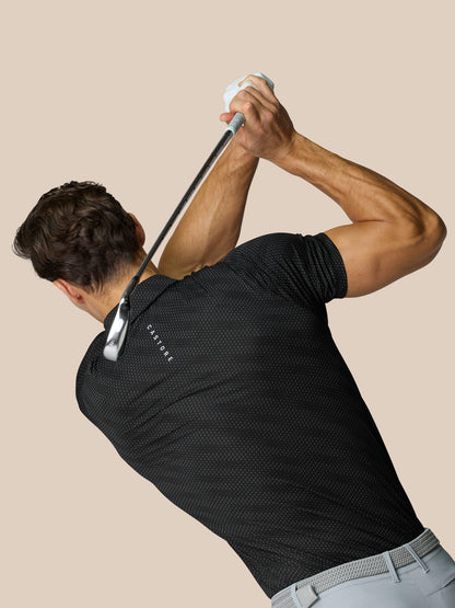 Male model wearing Club Graphic Polo Black with dotted texture during backswing holding a golf club