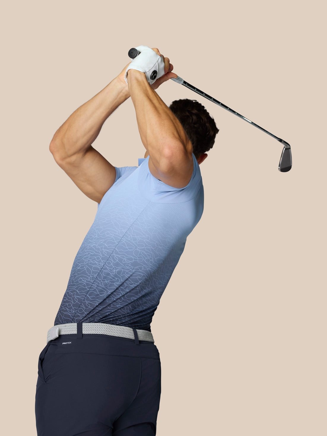 Side/back angle of golfer in sky blue Club Graphic Polo with ombre gradient, Castore branding at the neck, raising a golf club.