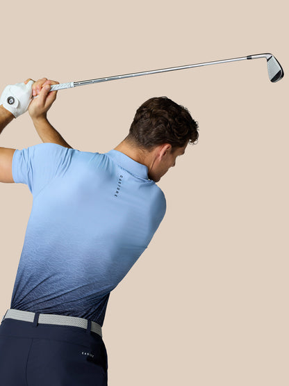 Back view of a golfer in sky blue Club Graphic Polo showing gradient pattern and Castore branding on the upper back, preparing to swing.