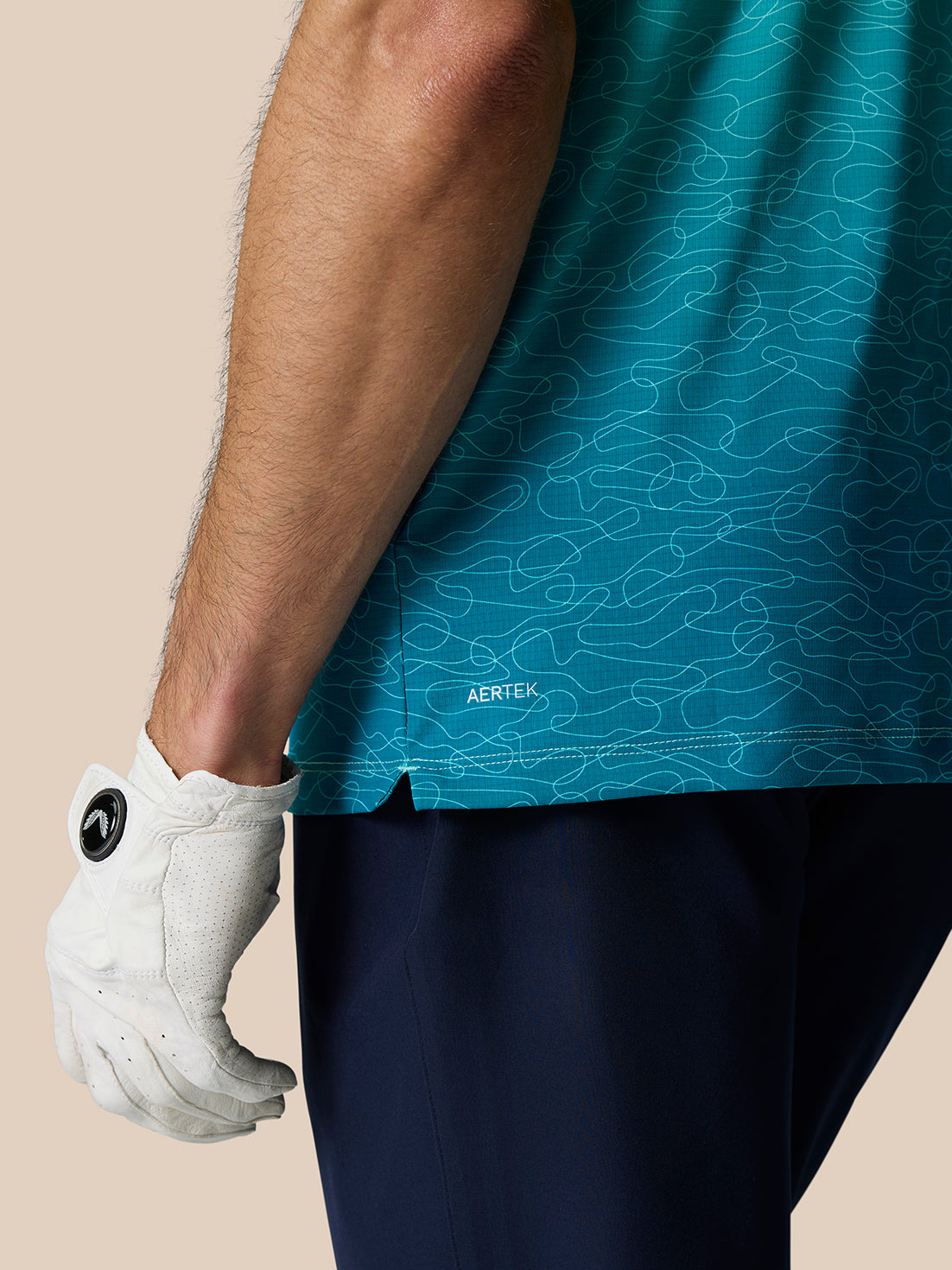 Close up of Club Graphic Polo in light aqua with teal ombre print and AERTEK branding at the hem, white golf glove visible.