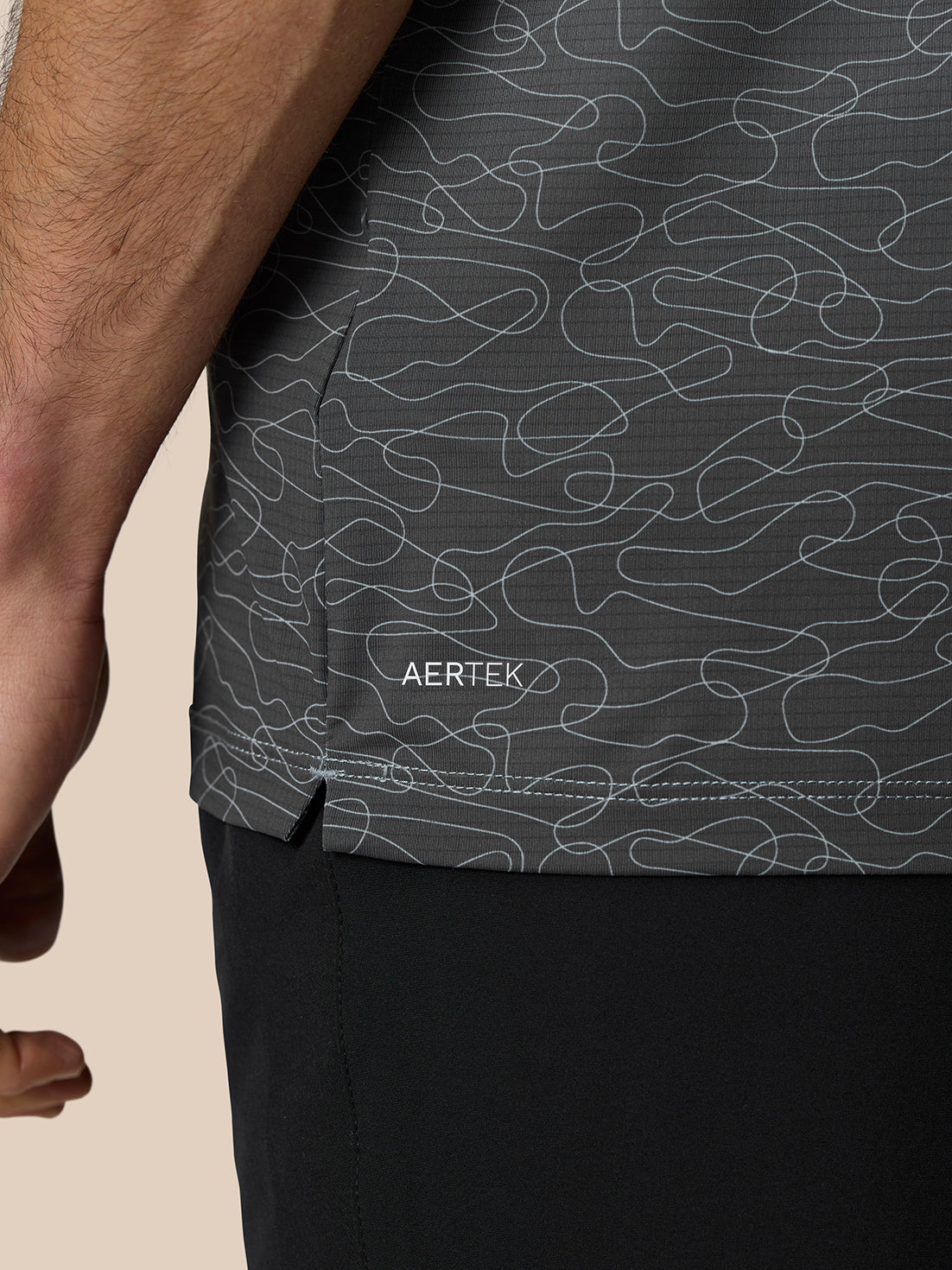 Close up of the polo hem showing abstract print and AERTEK branding near the side slit.
