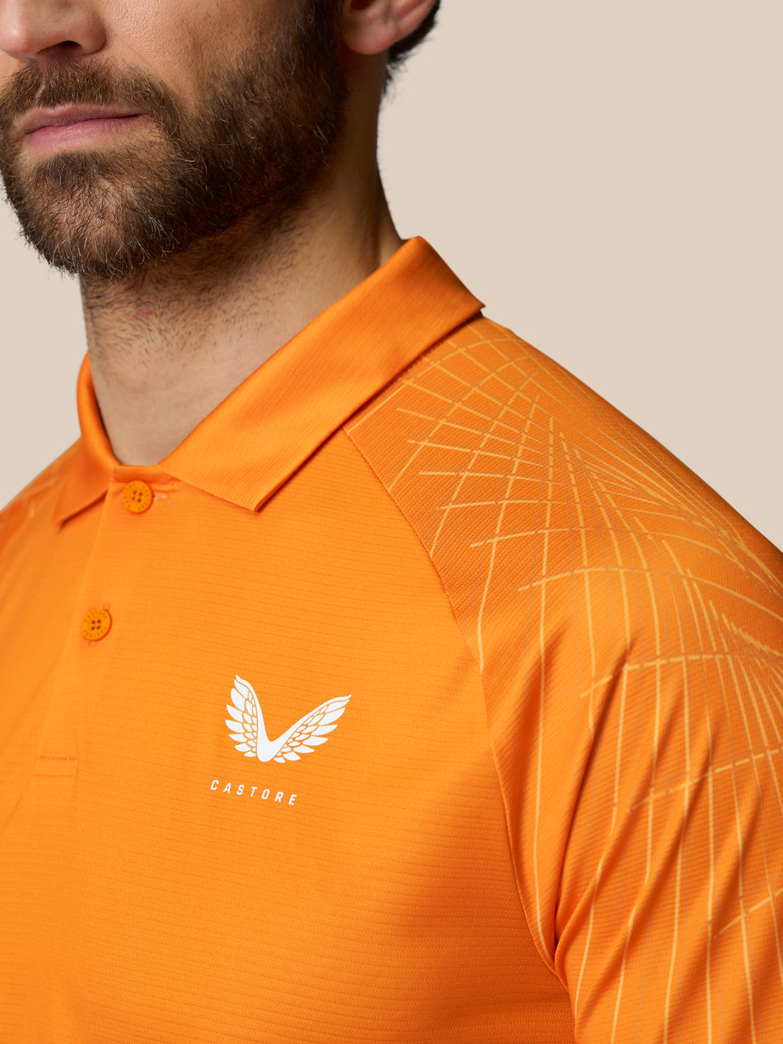 Close up of orange Club Geo Print Polo showing white Castore wing logo on left chest and geometric shoulder pattern