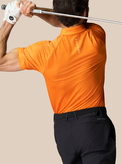 Back view of a man in an orange Club Geo Print Polo swinging a golf club overhead; Castore branding visible on the upper back.