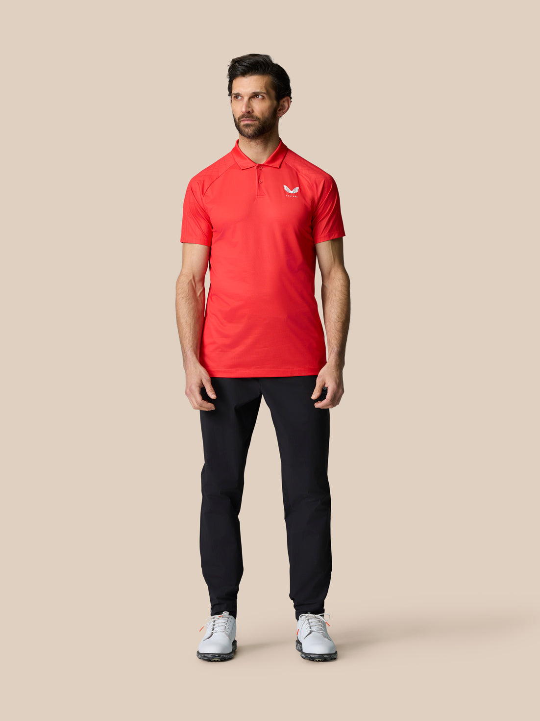 Male model wearing red Club Graphic Polo with white left chest logo, dark trousers, and white sneakers.