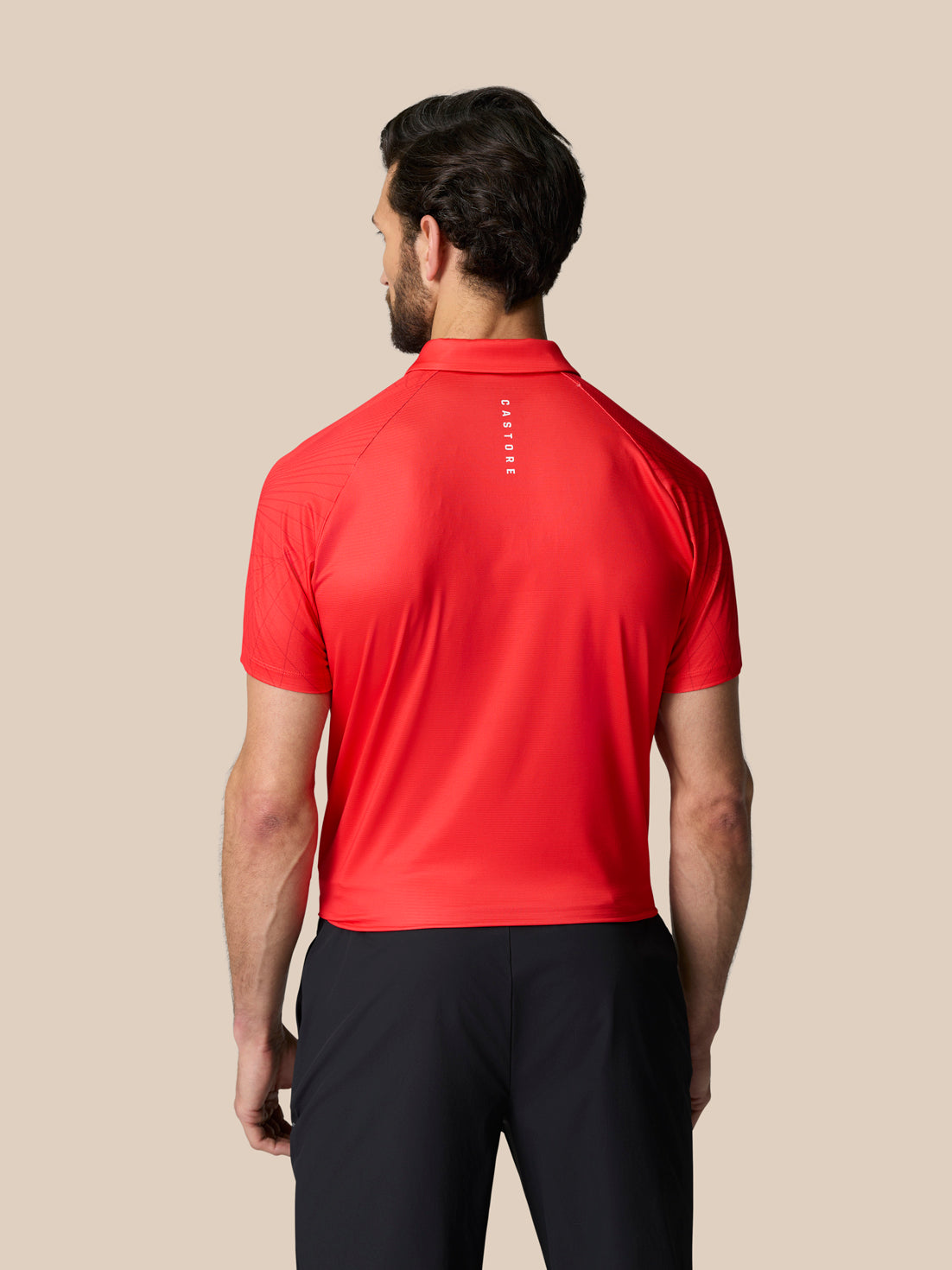 Back view of male model in red Club Graphic Polo with vertical Castore branding on the upper back.