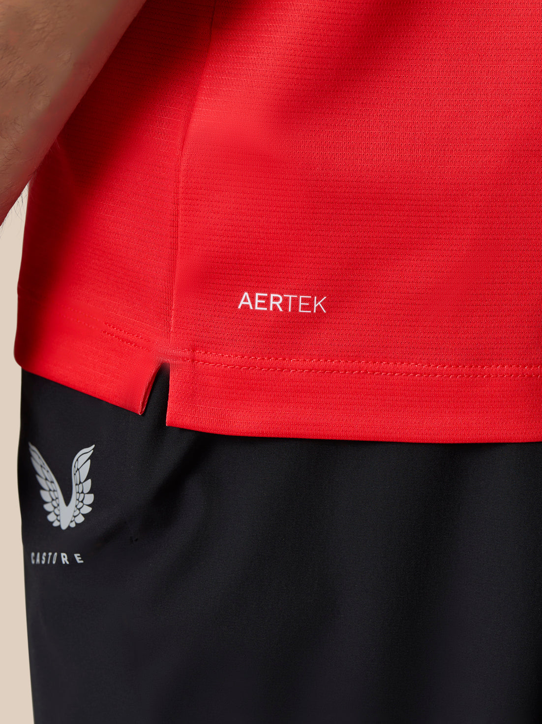 Close-up of a red AERTEK polo hem with Castore branding and wing logo on black shorts.