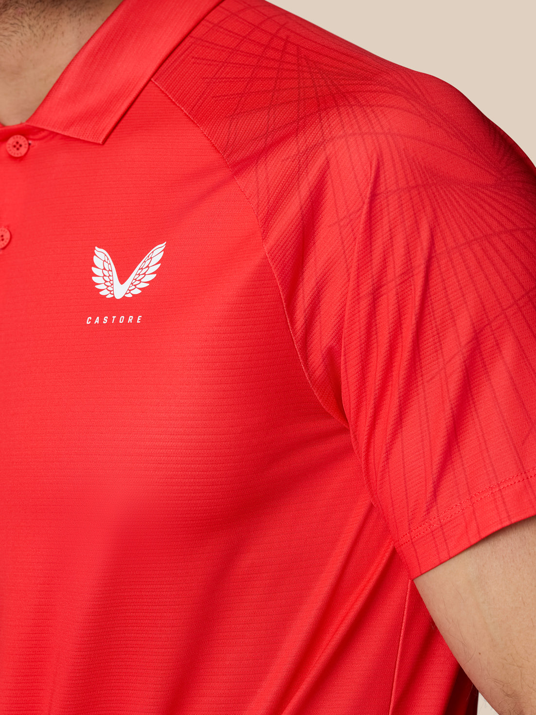 Close-up of red Club Graphic Polo fabric showing white Castore logo on the left chest.