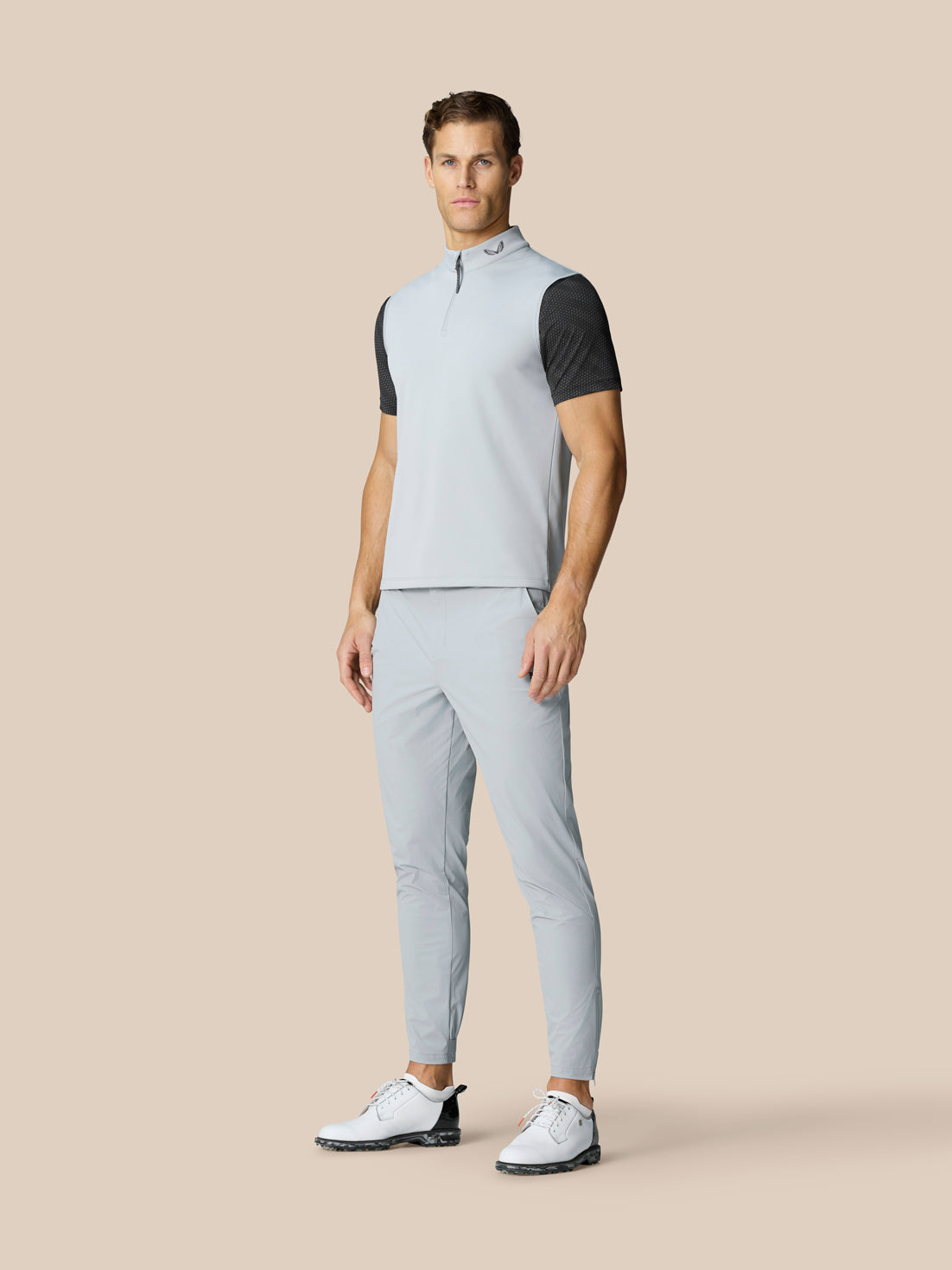 Male model wearing light grey Club Classic ½ Zip Gilet with a high neck, paired with matching trousers and white golf shoes.