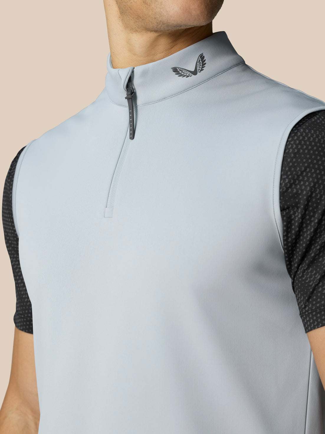 Close up of the light grey Club Classic half zip golf gilet showing a high collar with a front zipper and Castore logo on the neck with black dotted sleeves.