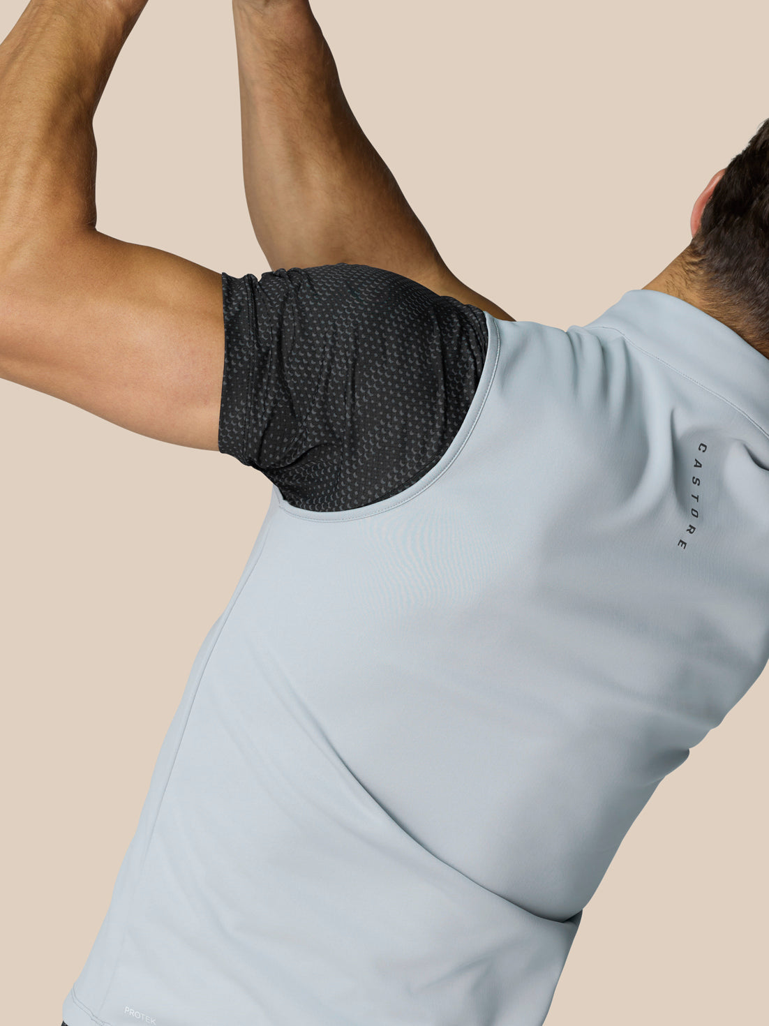 Side back view of a man in the light grey Club Classic half zip golf gilet over a black dotted sleeve, Castore lettering along the back neck.