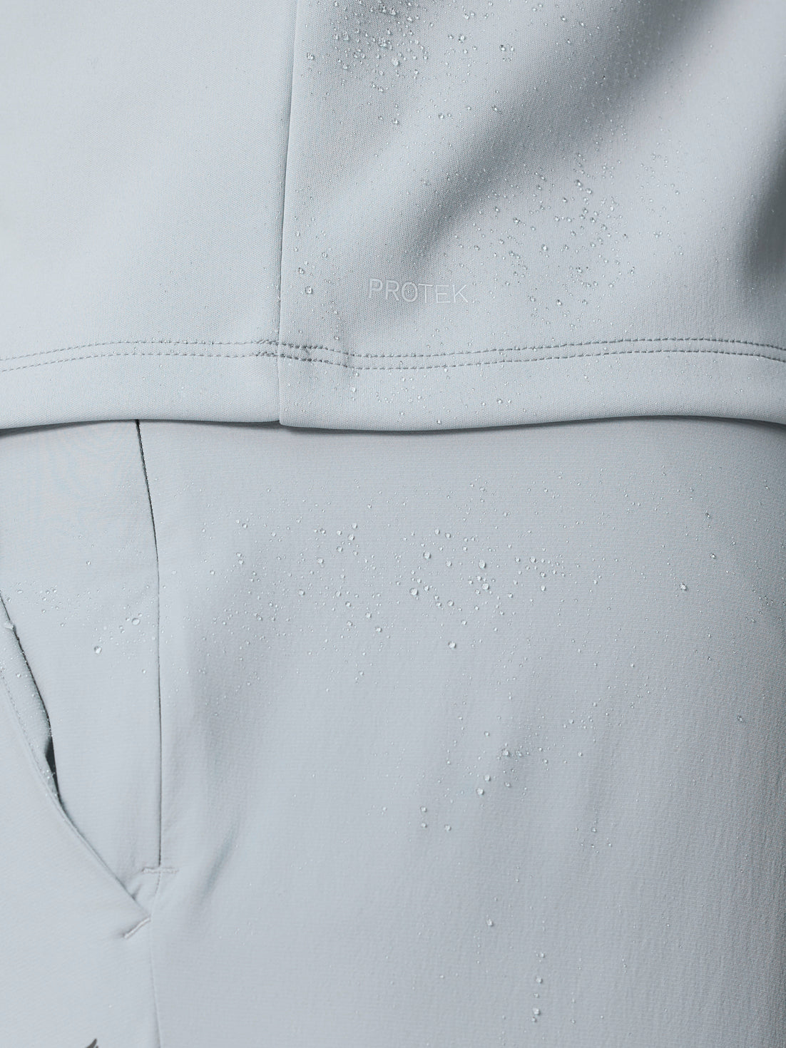 Close-up of light grey fabric with water droplets and PROTEK branding indicating the water resistant finish.