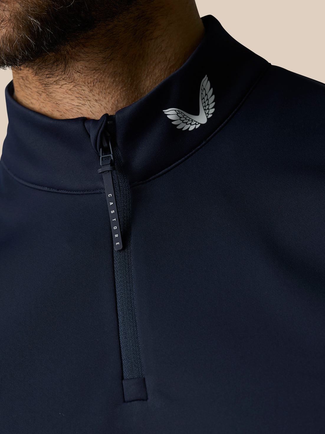 Close up of navy Club 1/2 Zip Gilet collar with zipper pull and Castore wing logo