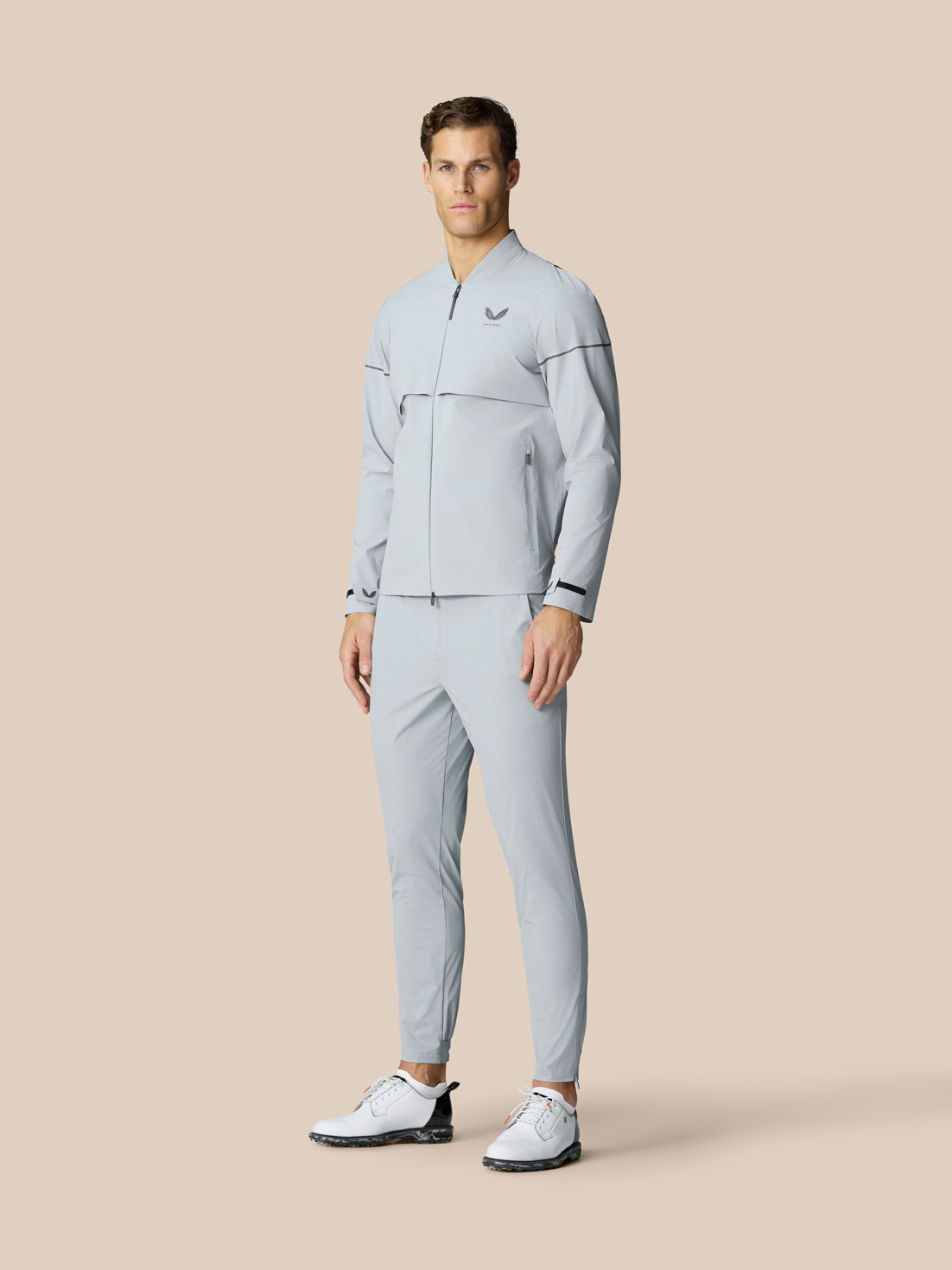 Full body view of a man in a light grey matching athletic jacket and pants set with zip front