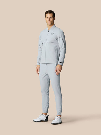 Full body view of a man in a light grey matching athletic jacket and pants set with zip front