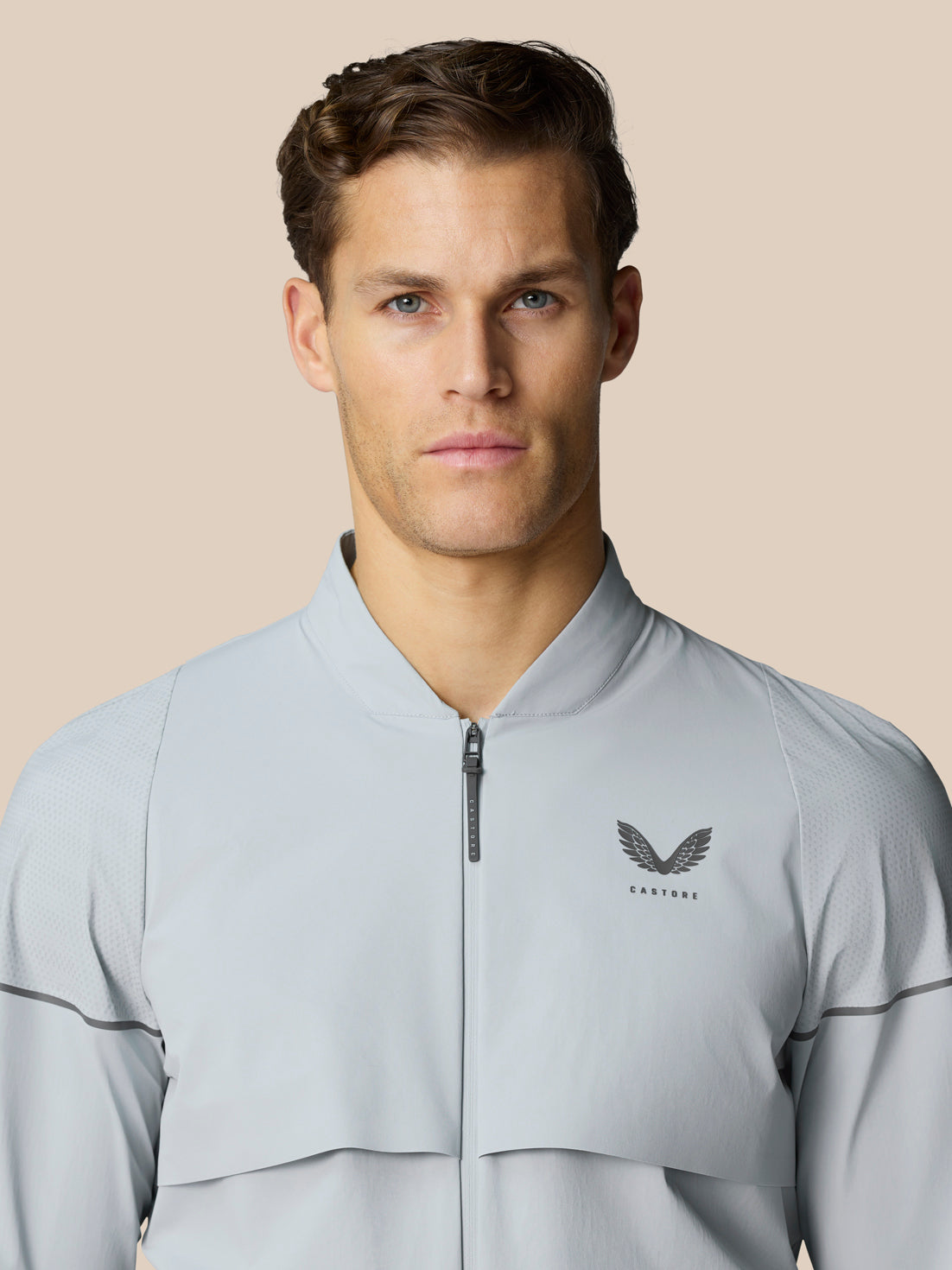 Male model wearing a light grey Golf Pinnacle LVS Woven Jacket with zip front and chest logo
