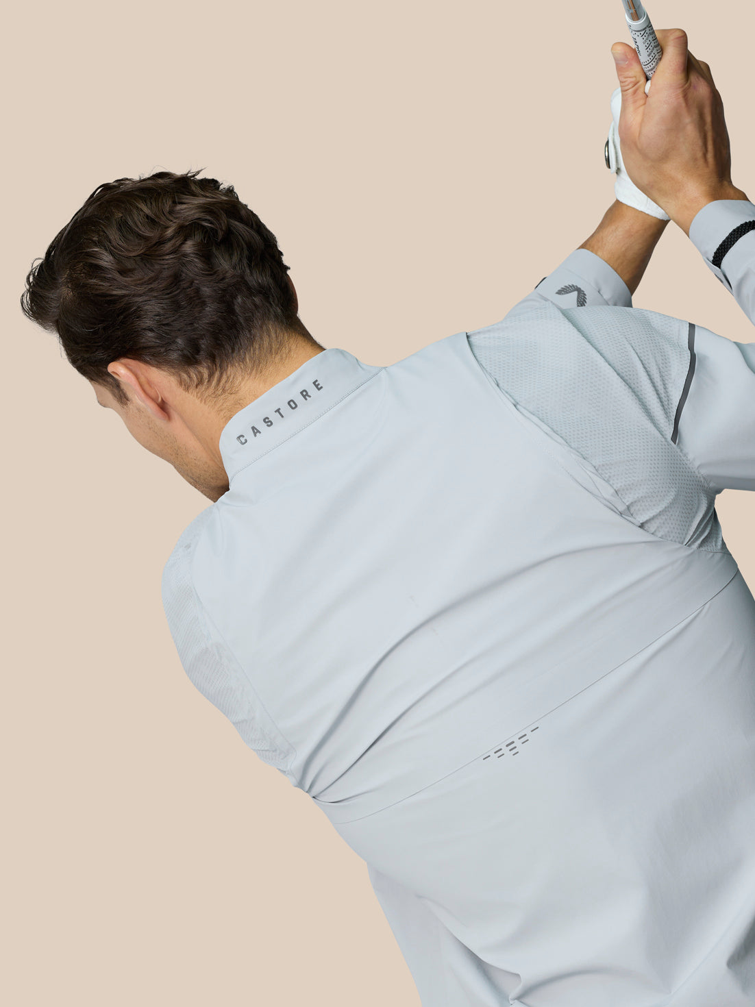 Back view of a model wearing the light grey Golf Pinnacle LVS Woven Jacket, showing vent details and Castore branding.