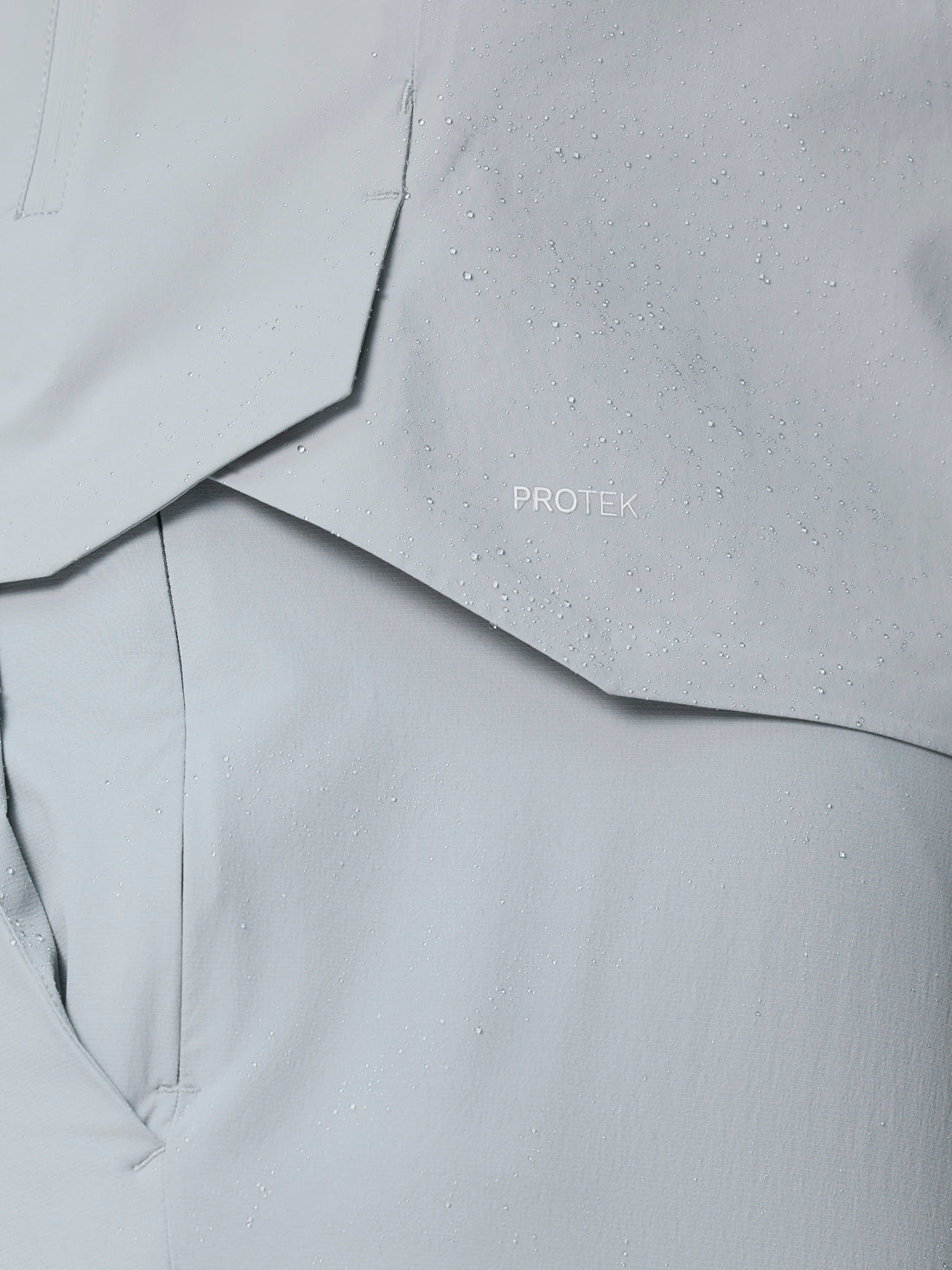 Close-up of light grey ProTek fabric from Golf Pinnacle LVS Woven Jacket with water droplets.