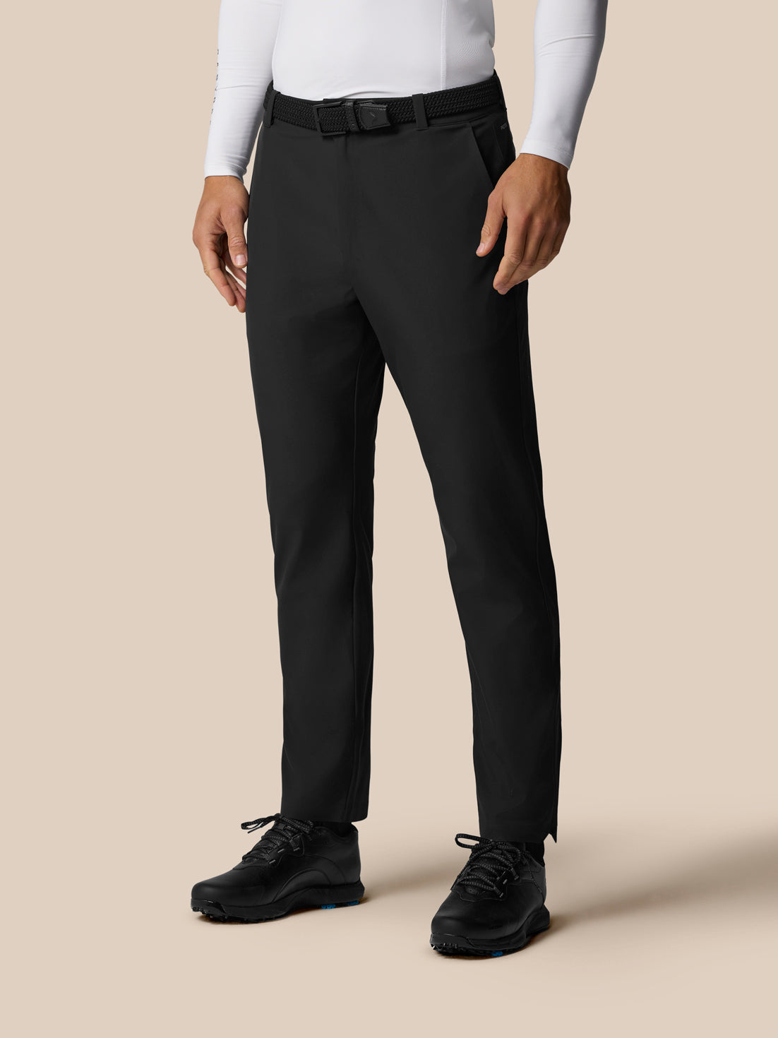 Male model wearing black Golf Pinnacle trousers with a woven belt and white top, full-length shot