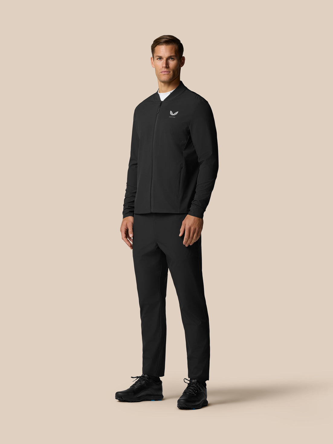 Male model wearing Castore Golf Pinnacle Trouser 32 Black Alloy with a black zip jacket