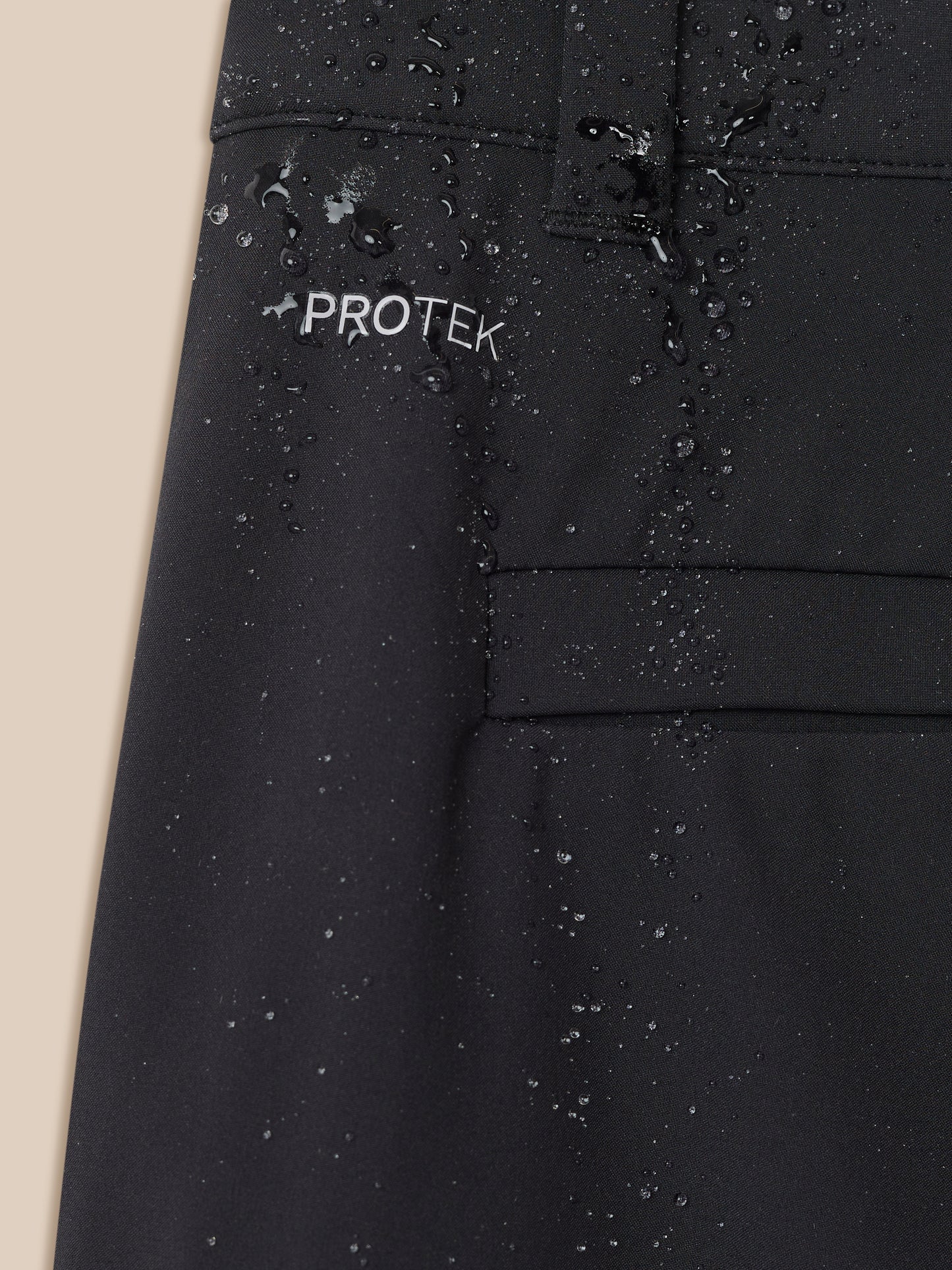 Close-up of black golf trouser fabric with water droplets and PROTEK logo