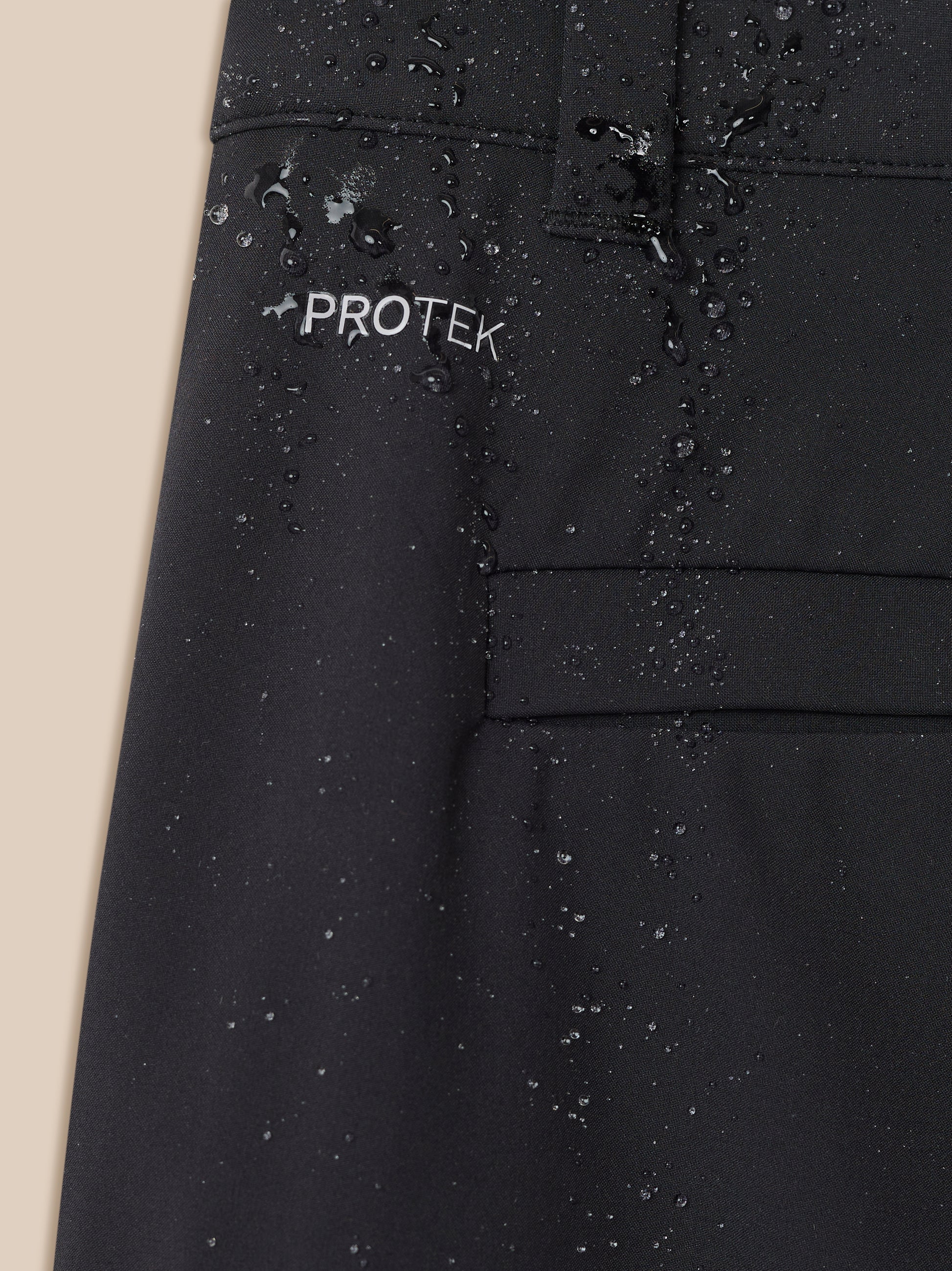 Close-up of black golf trouser fabric with water droplets and PROTEK logo
