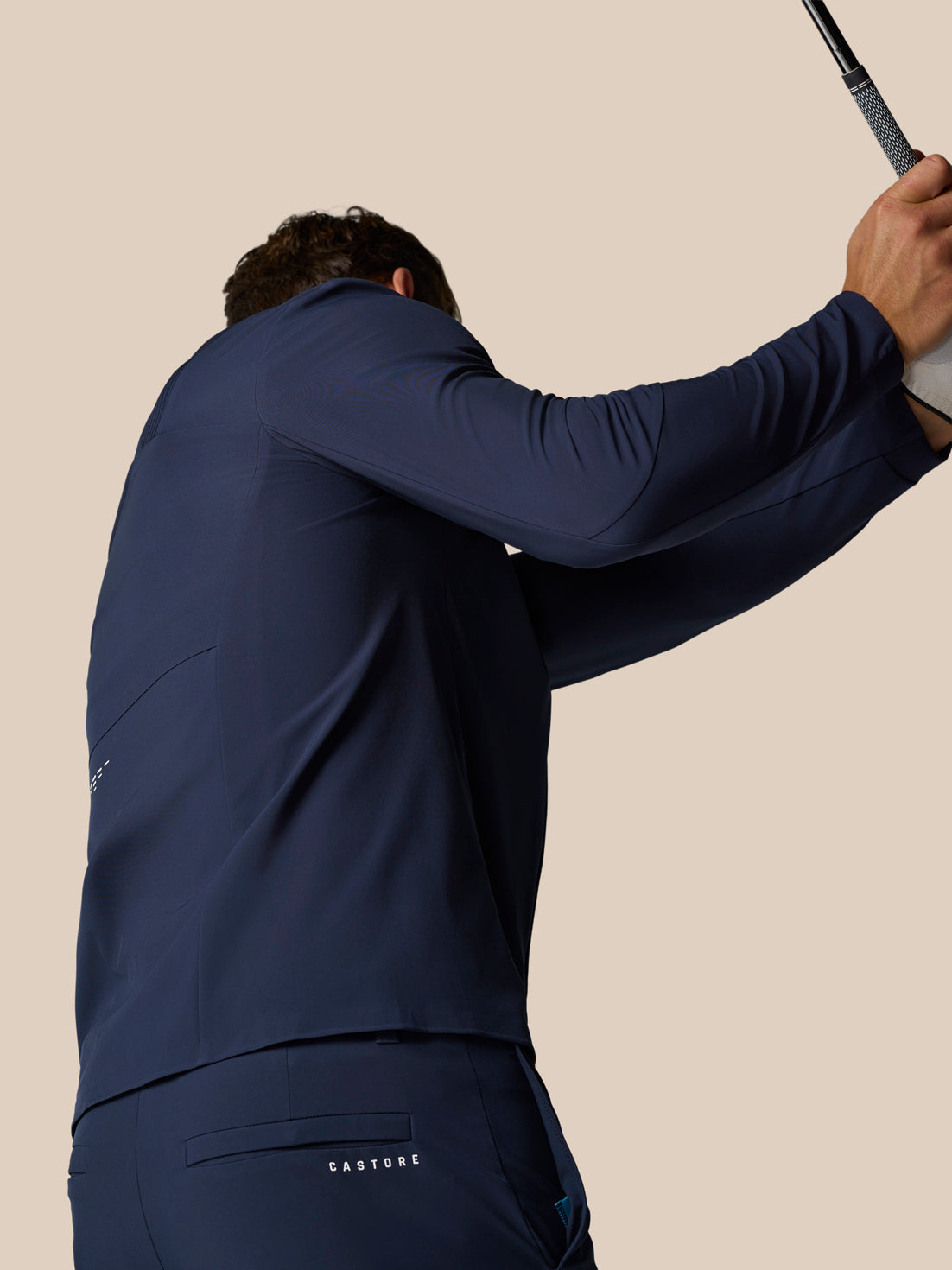 Back view of a model in midnight navy Castore golf wear holding a golf club overhead.