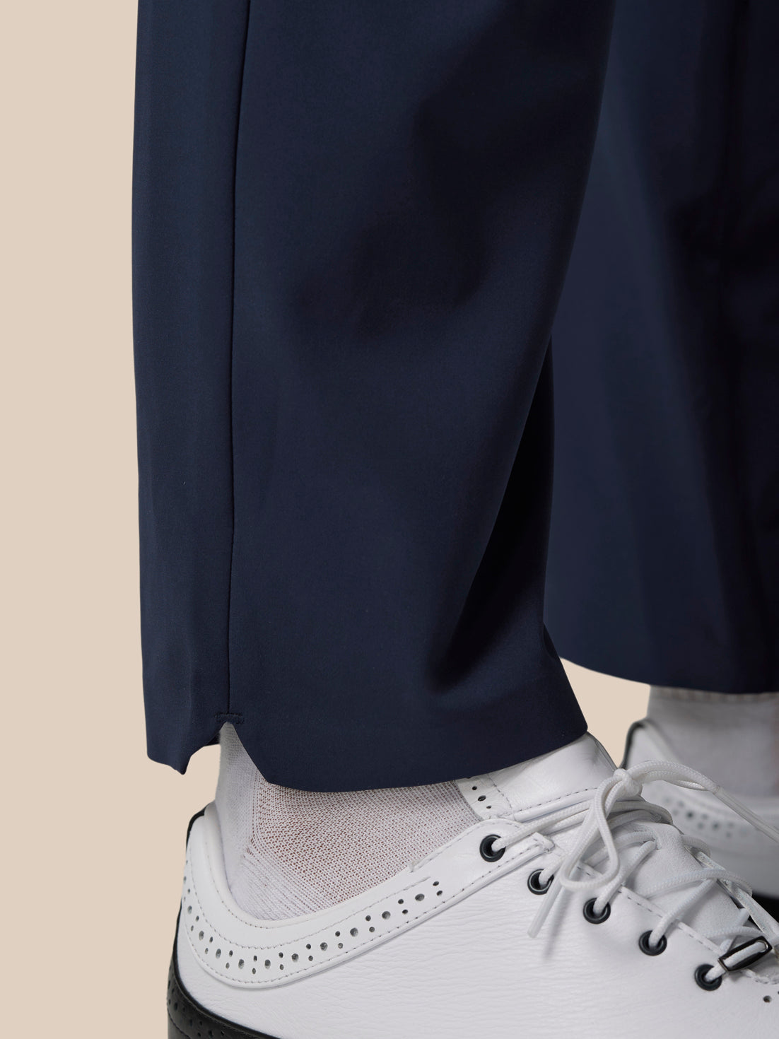 Close-up of navy trouser leg hem over white golf shoes with water droplets on the fabric.