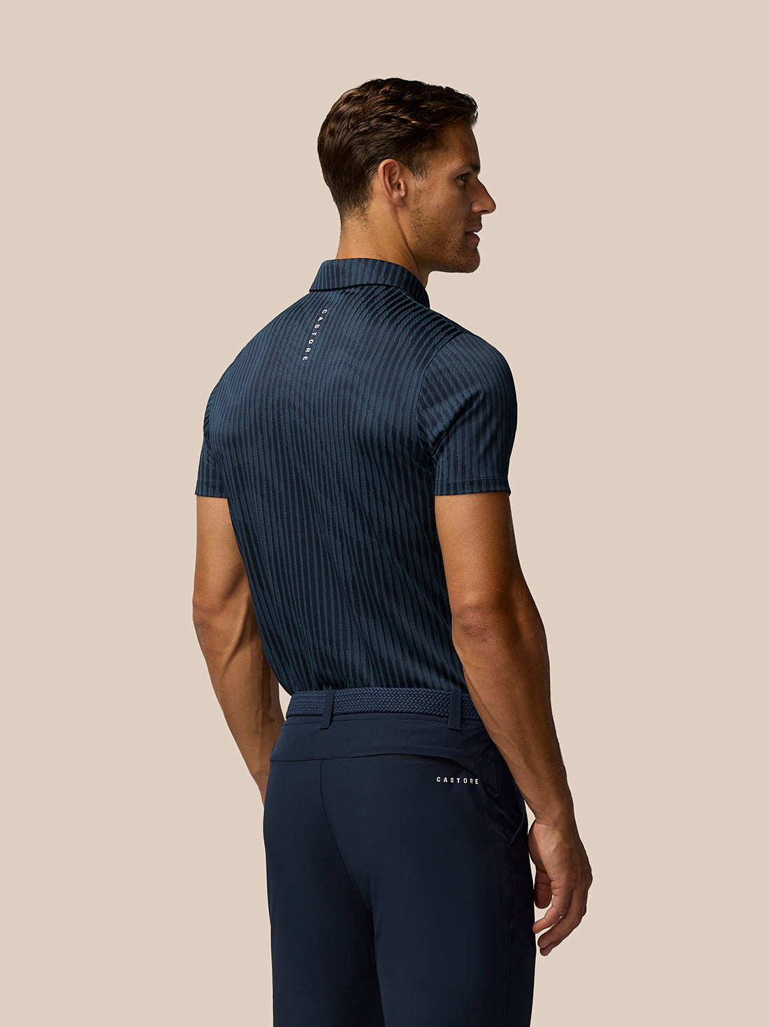 Back view of a man wearing a midnight navy striped polo with Castore logo on the upper back