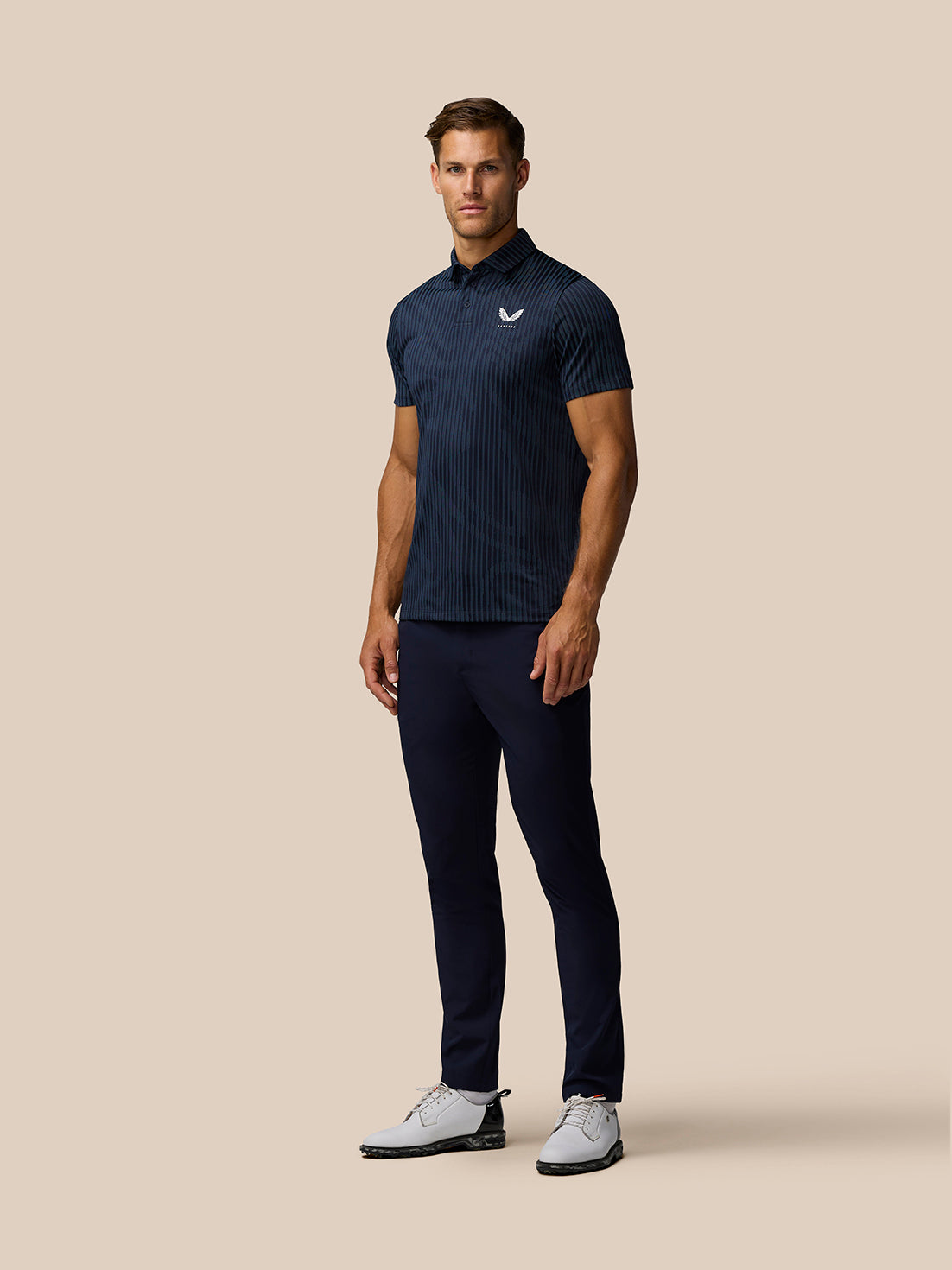 Male model wearing Golf Pinnacle Glow Polo in Midnight Navy with vertical stripes and Castore logo on chest