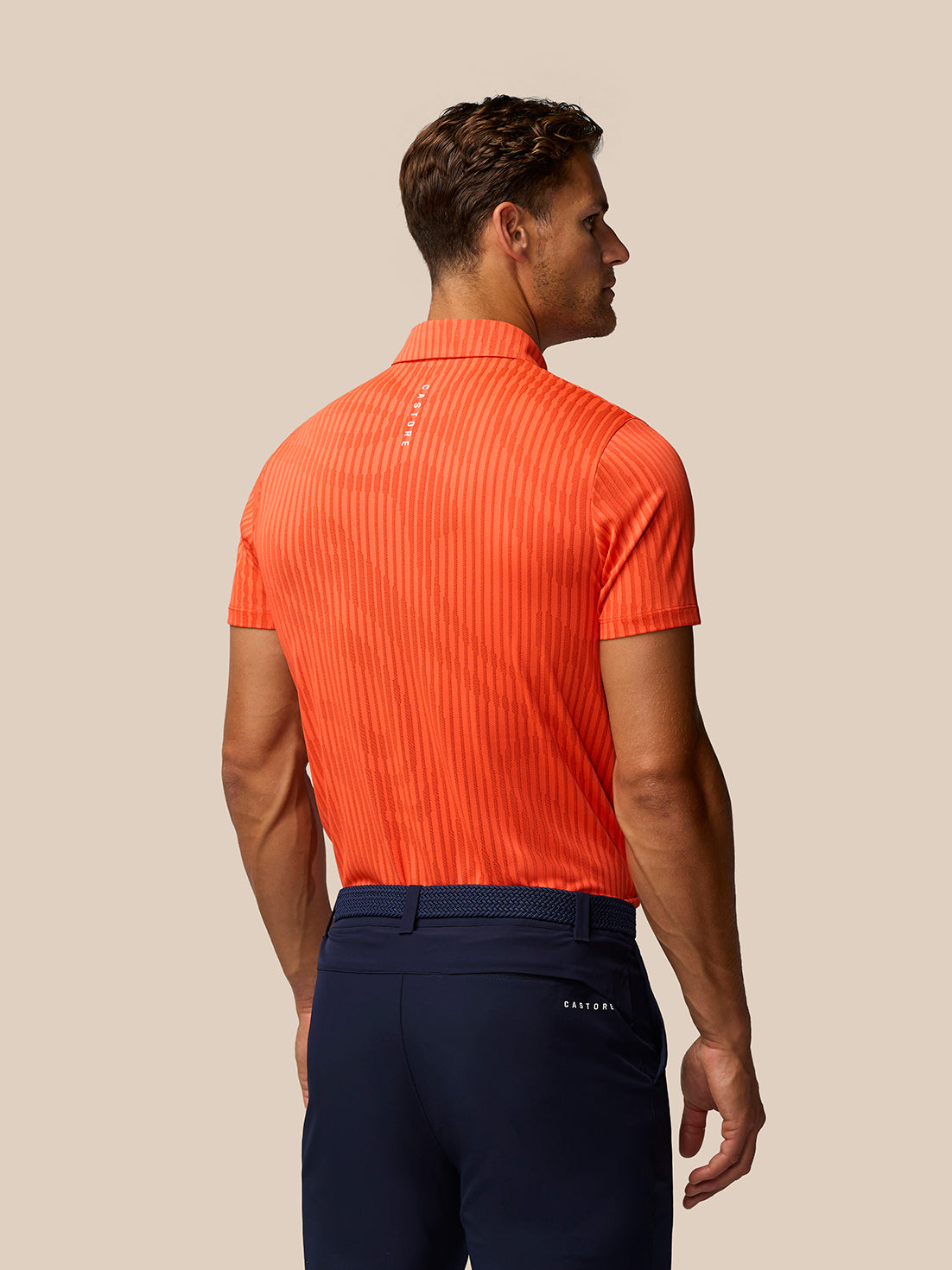 Back view of a male model in the bright orange striped Golf Pinnacle Glow Polo