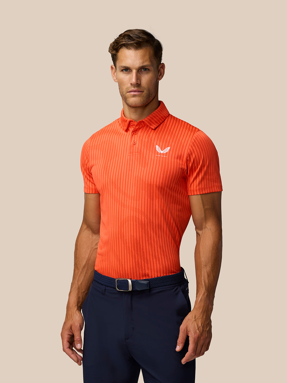 Male model wearing bright orange striped Golf Pinnacle Glow Polo with Castore logo on chest