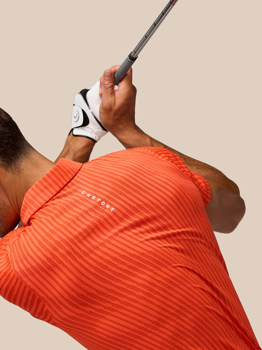Athlete wearing bright orange striped Golf Pinnacle Glow Polo mid swing with Castore logo on left chest