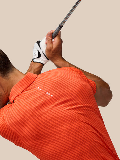 Athlete wearing bright orange striped Golf Pinnacle Glow Polo mid swing with Castore logo on left chest