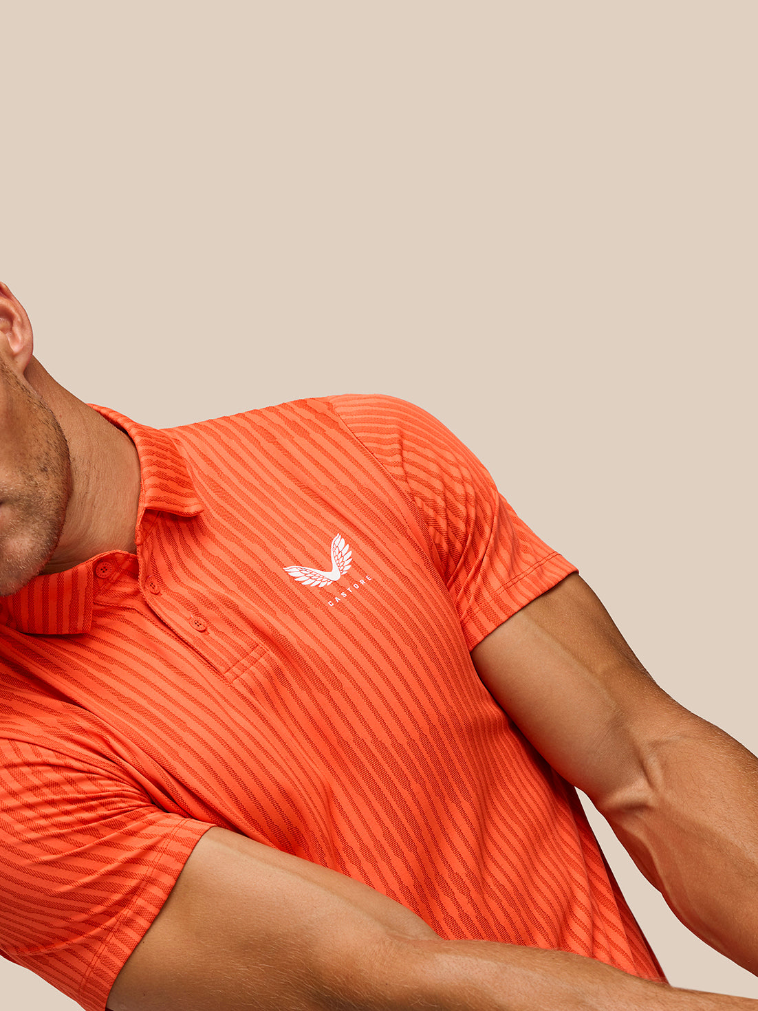 Model wearing bright orange striped Golf Pinnacle Glow Polo with Castore logo on left chest