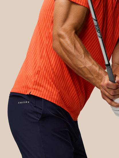Side view of a male golfer wearing the bright orange striped Golf Pinnacle Glow Polo while gripping a golf club