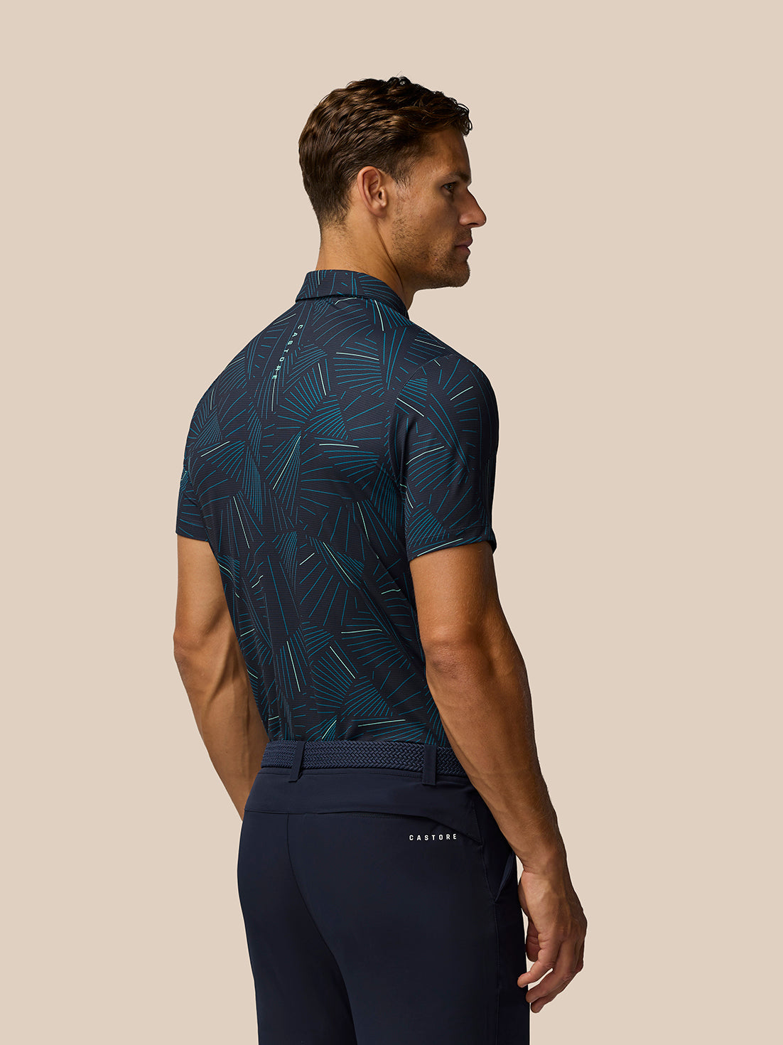 Back view of male model wearing midnight navy aqua print golf polo with belt and navy pants
