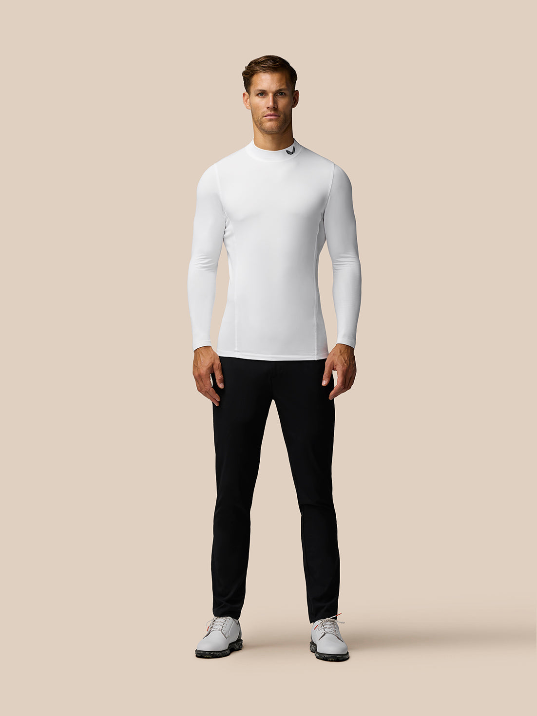 Front view of a man wearing a white Golf Club Long Sleeve Thermal Mock Neck top with black pants.