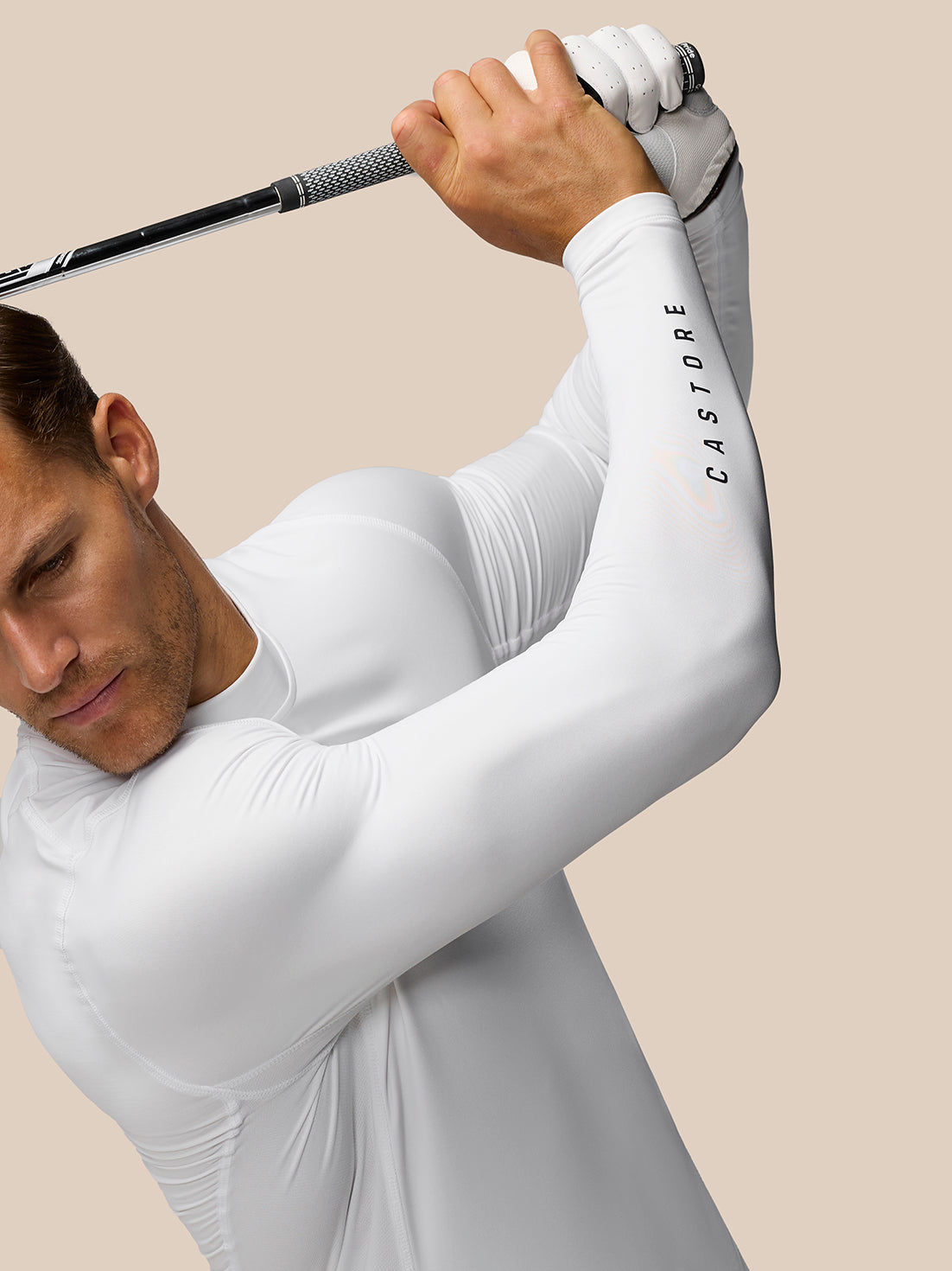 Golfer in a white Golf Club Long Sleeve Thermal Mock Neck top swings a club, Castore branding visible on the sleeve.