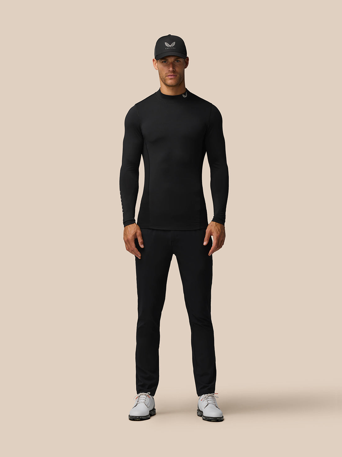 Front view of a man wearing the black Golf Club Long Sleeve Thermal Mock Neck top with cap and sneakers