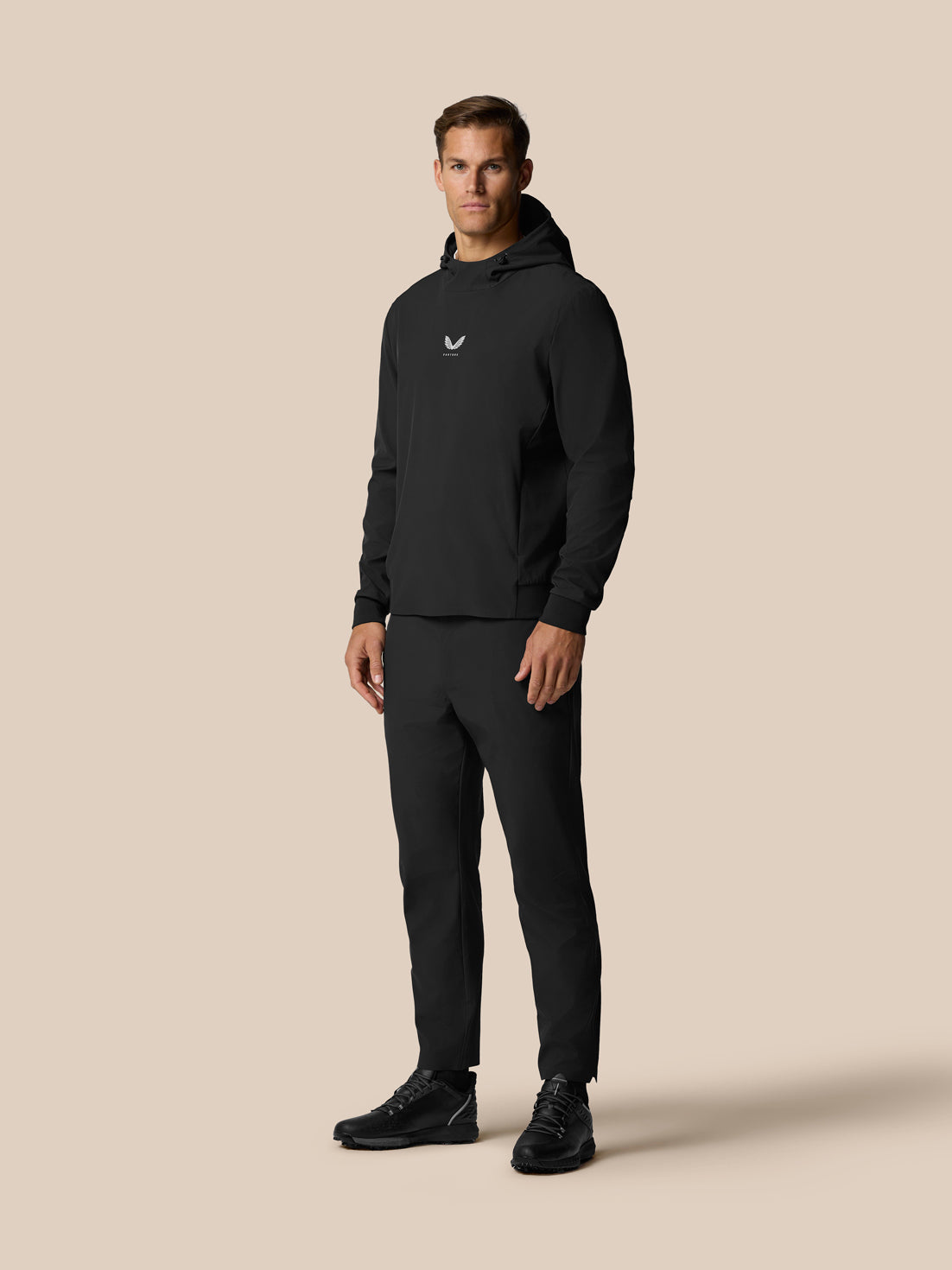 Male model wearing black Golf Pinnacle Performance Hoodie with hood up, black joggers, Castore logo on chest.