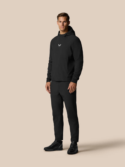 Male model wearing black Golf Pinnacle Performance Hoodie with hood up, black joggers, Castore logo on chest.