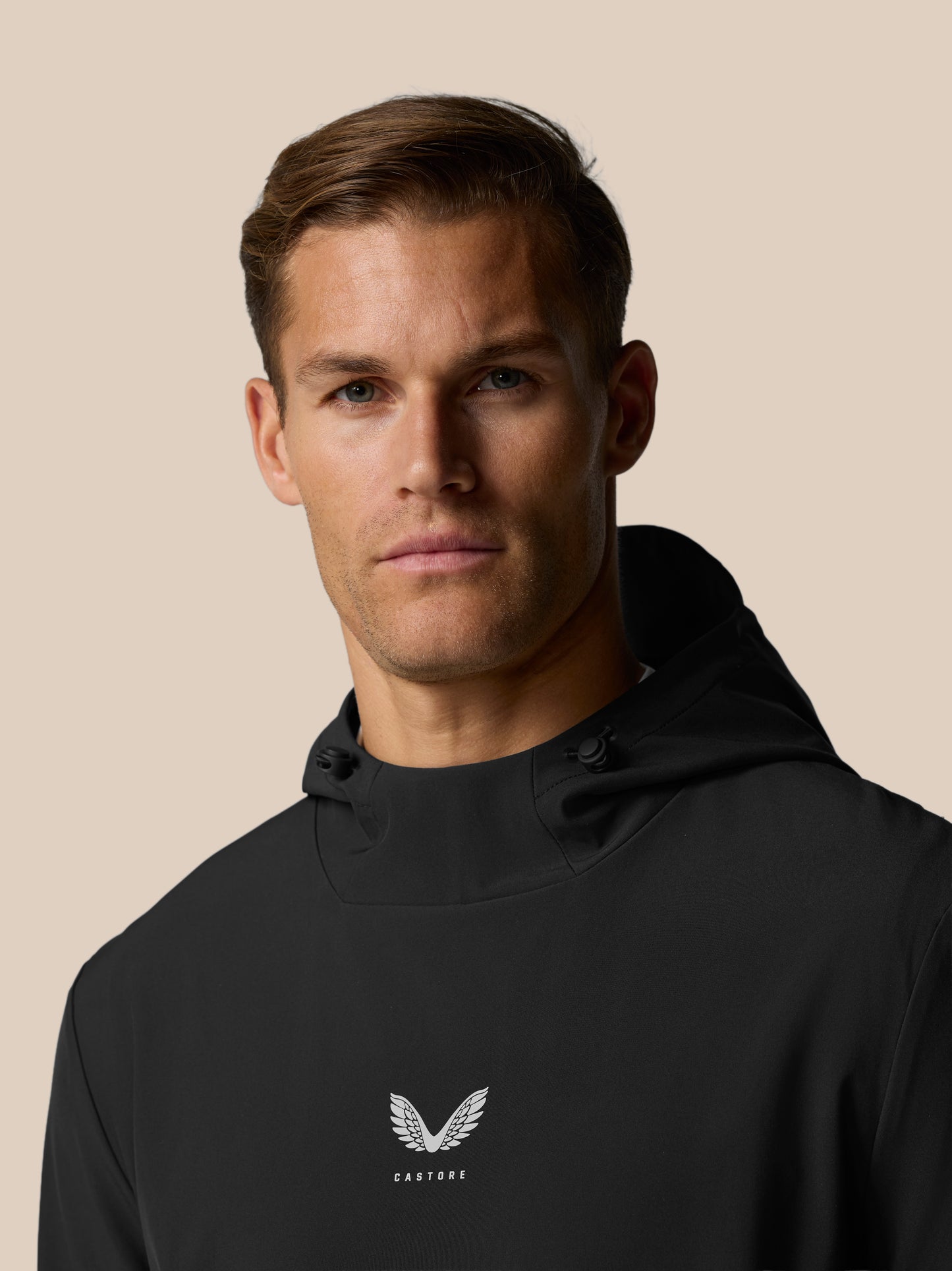 Side view of male model in black Golf Pinnacle Hoodie with hood and Castore logo on chest.