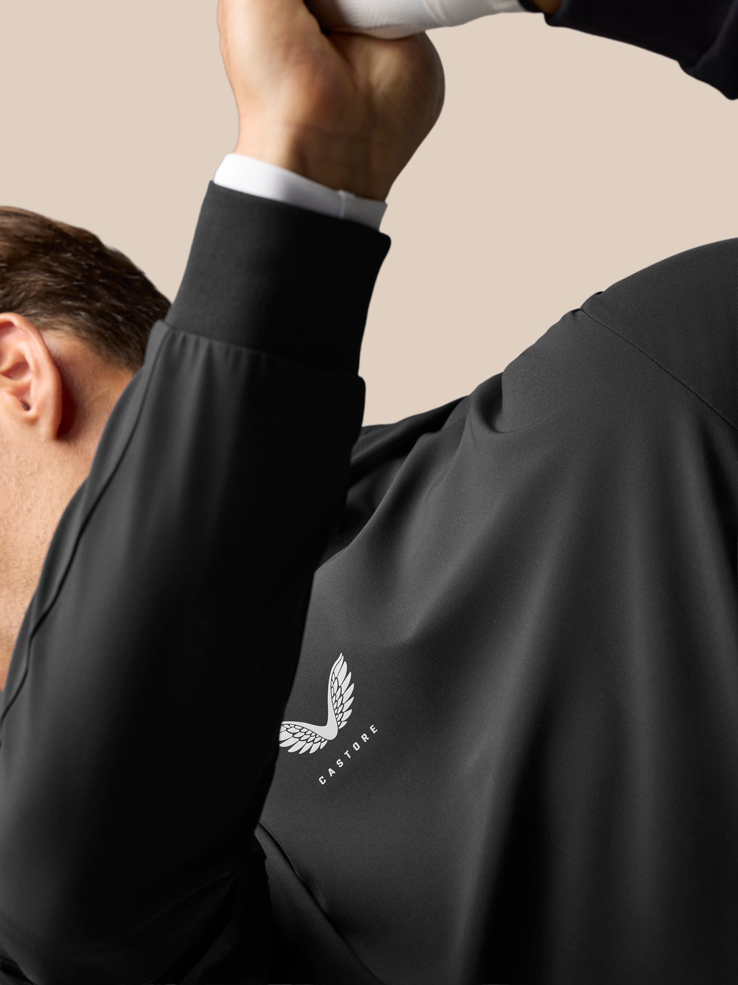 Close-up of male torso in black Golf Pinnacle Performance Hoodie showing Castore logo and wing emblem on chest.