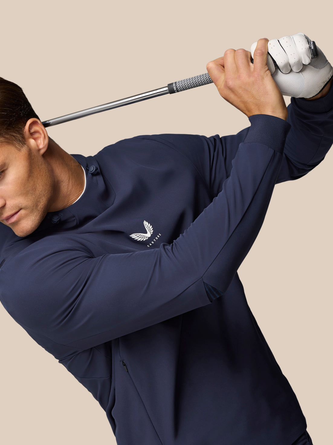 Male golfer in midnight navy Castore Golf Pinnacle Performance Hoodie mid swing with club raised and chest logo visible.