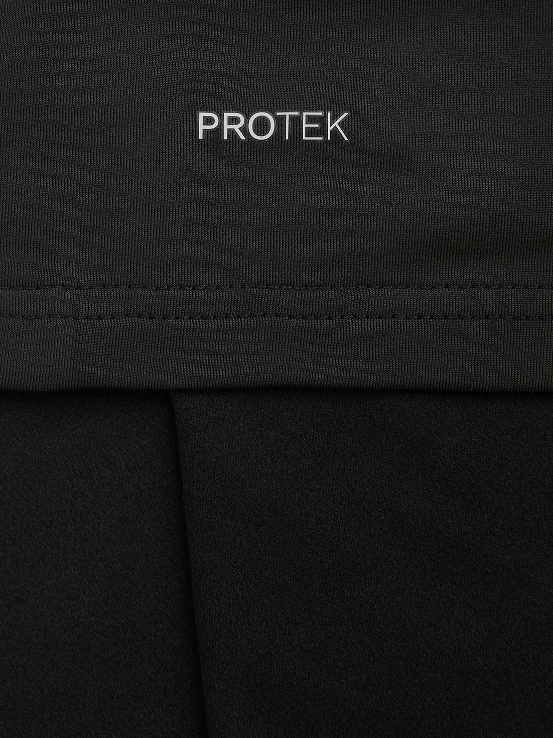 Close-up of black fabric with PROTEK branding and visible seam stitching
