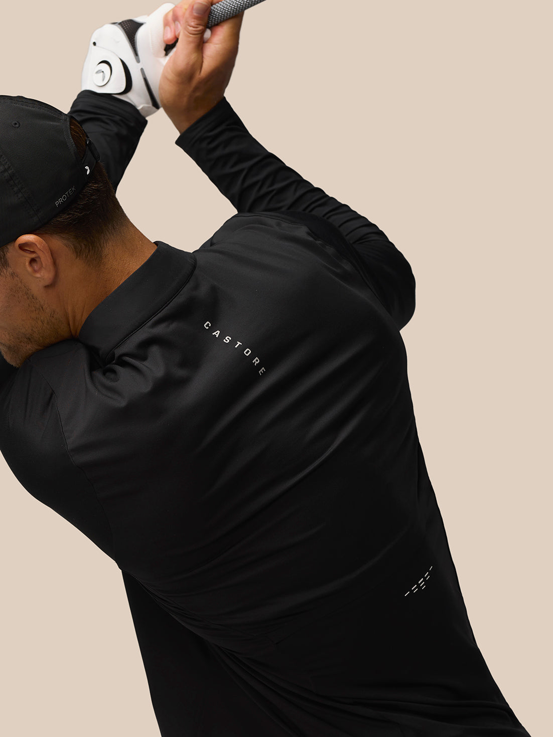 Back view of man in black Castore long sleeve golf top during swing with branding on back