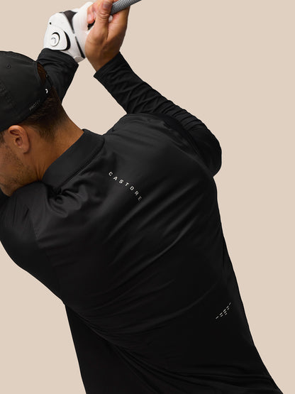 Back view of man in black Castore long sleeve golf top during swing with branding on back